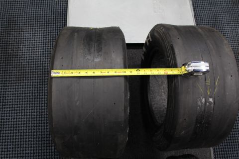 2003 Ford Crown Victoria - Two wide drag racing slicks side by side with a yellow tape measure stretched across their treads on a gray floor.