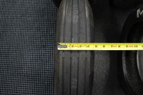 2003 Ford Crown Victoria - narrow ribbed drag front-runner tire with a yellow tape measure spanning its tread, on a gray floor.