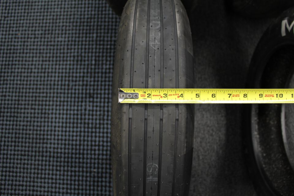 Narrow ribbed drag tire measured with a yellow tape measure on gray floor