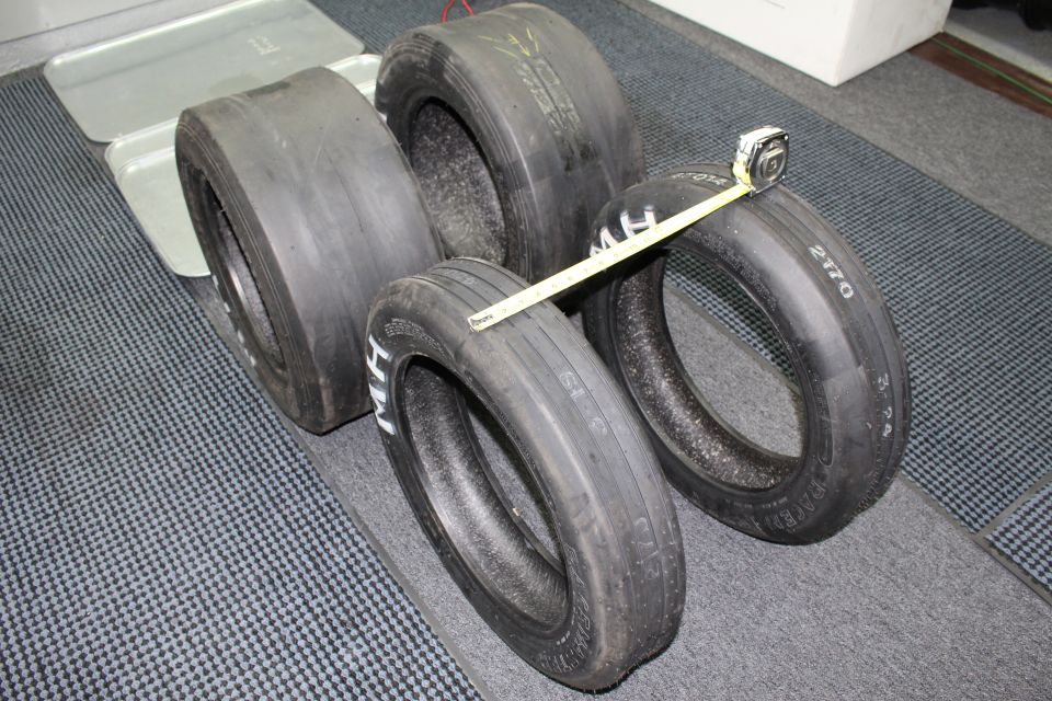 Four drag tires with M H lettering and a tape measure across them