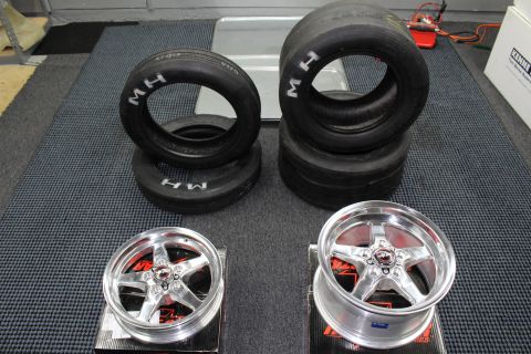 2003 Ford Crown Victoria - Stacked drag racing tires with white "M H" lettering displayed above two polished five-spoke aluminum wheels.