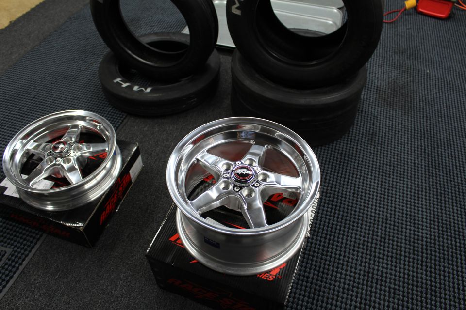 Two polished Race Star five-spoke wheels in front of stacked drag tires