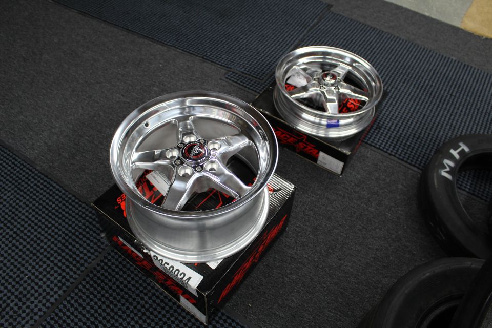 Two polished Race Star five-spoke wheels on boxes beside M/H tire