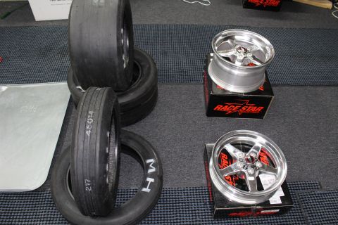 2003 Ford Crown Victoria - Stacked M/H drag tires sit beside two polished Race Star five-spoke wheels on boxes in a garage.