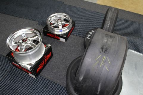 2003 Ford Crown Victoria - Two polished Race Star five-spoke wheels rest on boxes beside a large M/H drag slick on a garage floor.