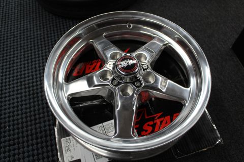 2003 Ford Crown Victoria - polished five-spoke aluminum wheel sits face-up on a black Race Star box with red graphics on a textured floor.
