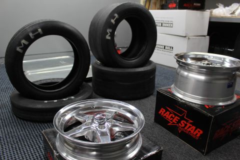 2003 Ford Crown Victoria - Two polished aluminum drag wheels rest near upright M/H tires and a Race Star Industries box on a carpeted floor.