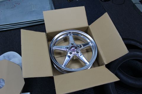 2003 Ford Crown Victoria - polished five-spoke aluminum drag wheel rests face-up inside an open cardboard shipping box.