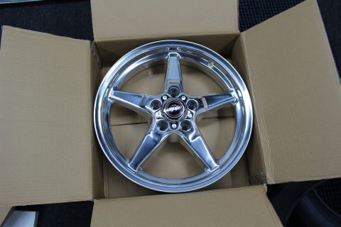 2003 Ford Crown Victoria - top-down view of a polished five-spoke aluminum drag wheel with a logo center cap inside a cardboard box.