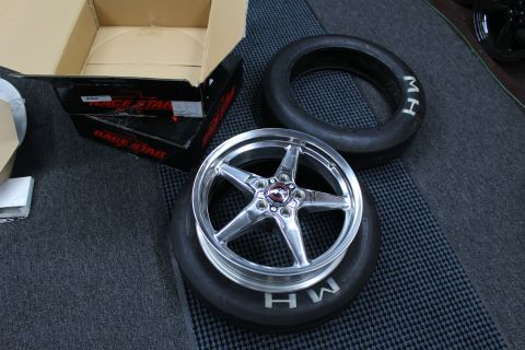 2003 Ford Crown Victoria - polished five-spoke drag wheel sits inside an M/H drag tire beside a Race Star box and a second tire.