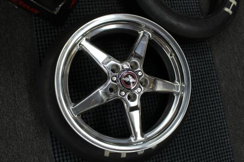 2003 Ford Crown Victoria - polished five-spoke aluminum drag wheel with a red center cap lies face-up on a tire on a dark floor mat.