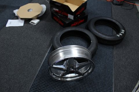 2003 Ford Crown Victoria - polished five-spoke drag wheel rests on its edge near M/H drag tires and black Race Star boxes on a mat.
