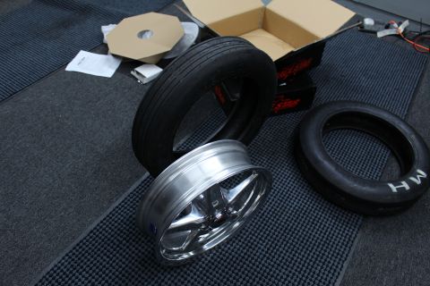 2003 Ford Crown Victoria - polished aluminum wheel barrel sits between M/H drag tires near an open box and a Race Star carton on a mat.