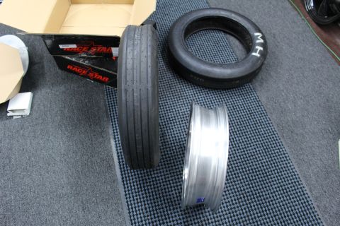2003 Ford Crown Victoria - narrow front-runner tire, an M/H drag tire and a polished wheel barrel rest on a mat beside a Race Star box.
