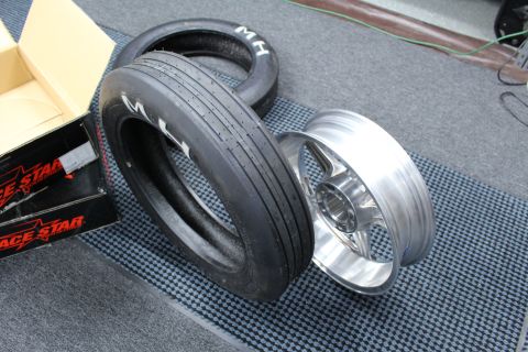 2003 Ford Crown Victoria - M/H drag slick tire and a polished aluminum wheel lie on their sides on a dark floor mat by a Race Star box.