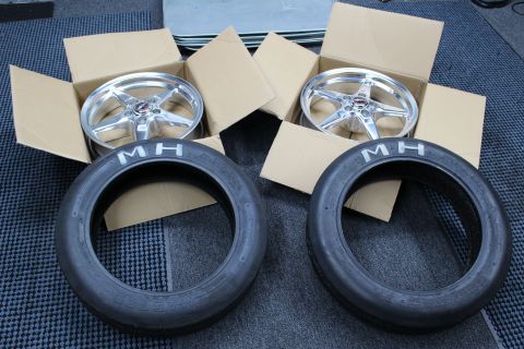 2003 Ford Crown Victoria - Two polished five-spoke drag wheels sit in open boxes above a pair of M/H drag tires on a mat.