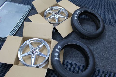2003 Ford Crown Victoria - Two polished five-spoke drag wheels rest in open boxes next to two M/H drag tires on a textured floor.