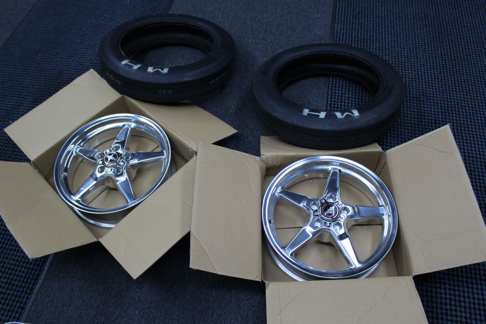 Two polished 5-spoke wheels in open boxes with M/H tires above