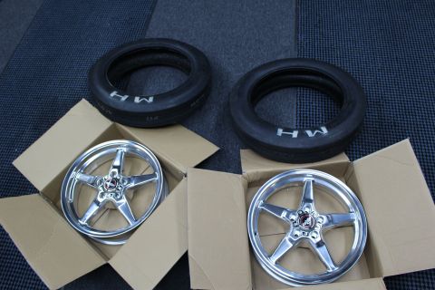 2003 Ford Crown Victoria - pair of polished five-spoke drag-racing wheels sit in cardboard boxes next to two MH-branded skinny front-runner tires.