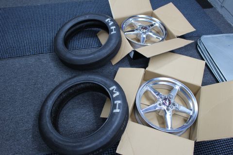 2003 Ford Crown Victoria - Two MH-lettered skinny front tires lie beside two boxed polished five-spoke drag wheels on a dark studio mat.