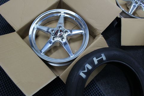 2003 Ford Crown Victoria - polished five-spoke aluminum drag wheel rests in a cardboard box next to an MH-branded skinny tire.