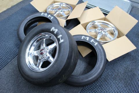 2003 Ford Crown Victoria - polished five-spoke wheel mounted on an MH drag slick leans against loose MH tires and two boxed wheels.