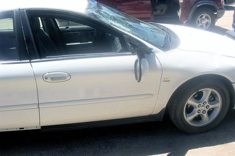 2000 Ford Taurus - A side profile of a white 2000 Ford Taurus shows its damaged windshield and a maroon SUV in the background.