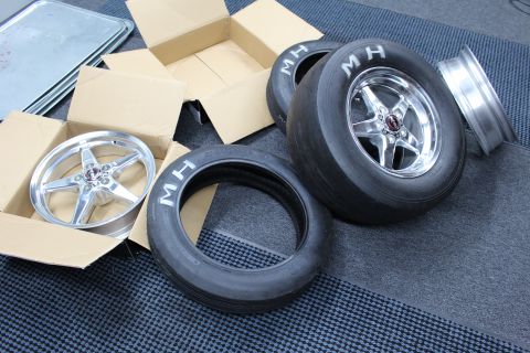 2003 Ford Crown Victoria - polished five-spoke wheel mounted on an MH slick lies near a boxed bare wheel and loose MH tires.