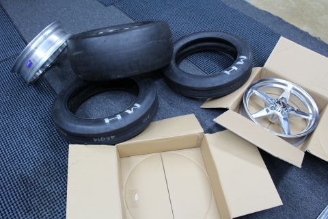 2003 Ford Crown Victoria - bare polished drag wheel and stacked MH slicks lie on a mat beside a boxed five-spoke wheel.
