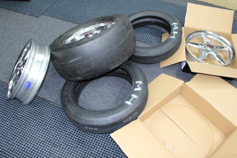 2003 Ford Crown Victoria - Stacked drag slicks and skinny MH tires sit beside polished five-spoke wheels and cardboard boxes.