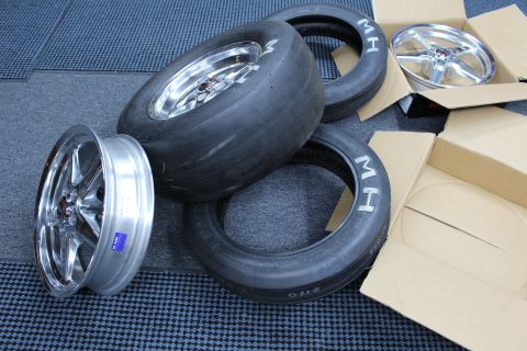 2003 Ford Crown Victoria - pile of MH drag slicks and skinny tires surrounds three polished five-spoke wheels on a dark mat.