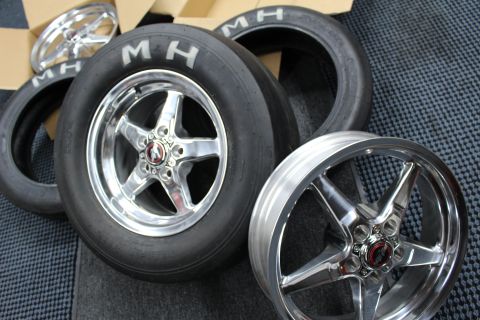 2003 Ford Crown Victoria - Two polished five-spoke wheels mounted on MH drag slicks lean together over a checkered studio mat.