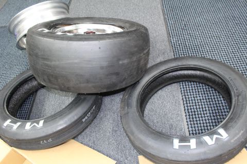 2003 Ford Crown Victoria - wide drag slick mounted on a polished wheel rests atop two skinny MH front tires on a patterned mat.