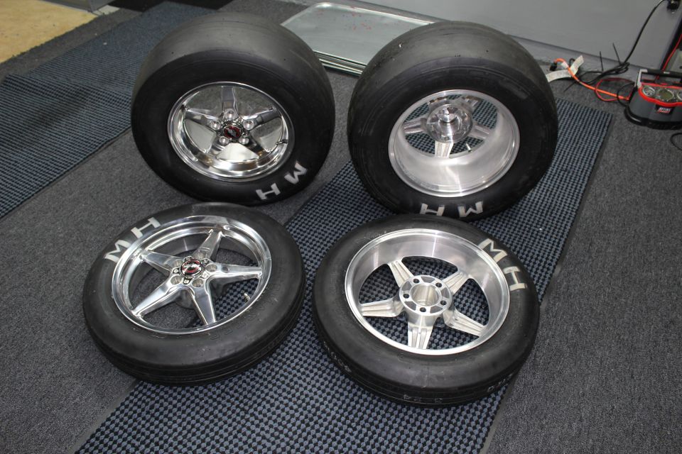 Four polished drag wheels mounted on MH slicks arranged on a dark mat