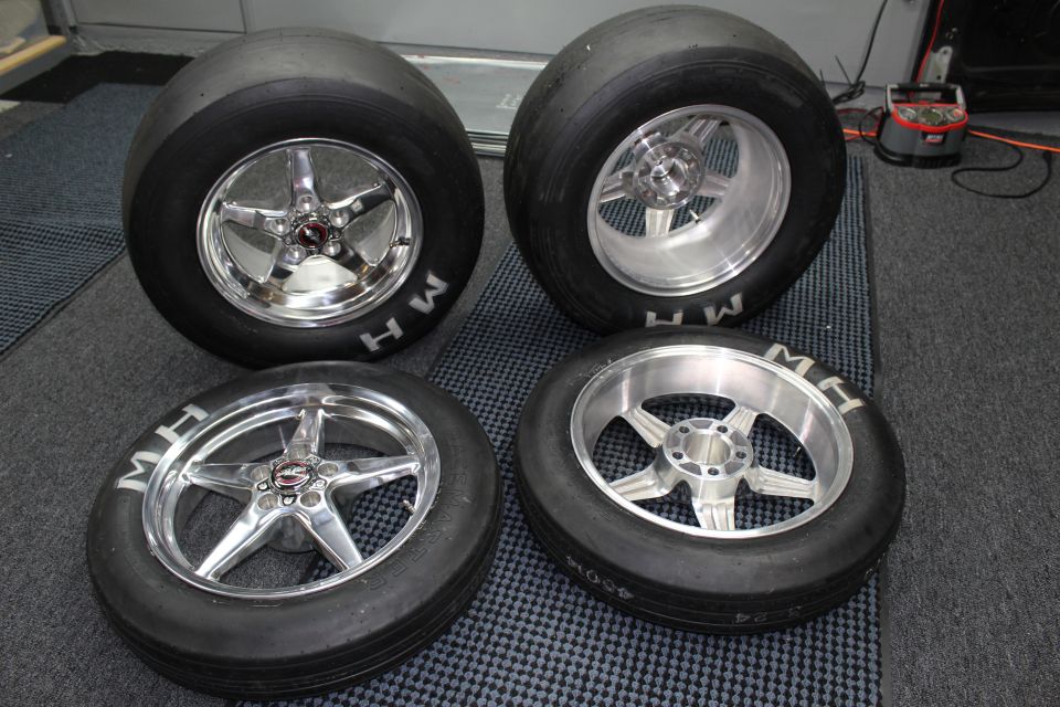 Four mounted MH drag slicks on polished wheels in a garage setting
