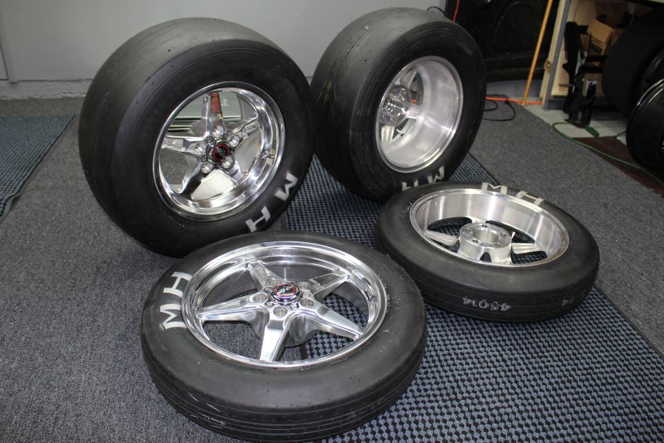 Four mounted MH drag tires on polished and machined wheels in a garage