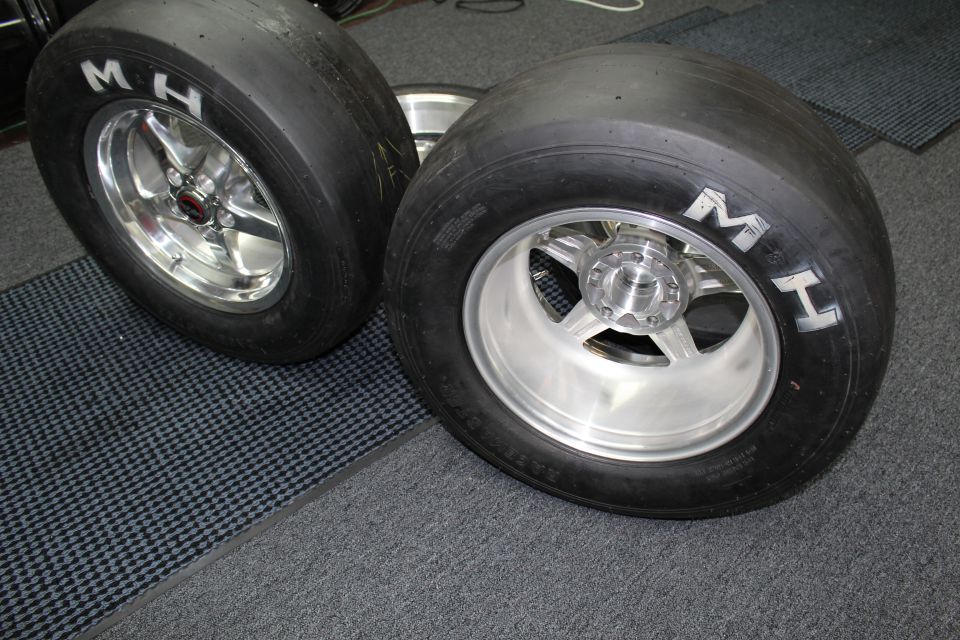 Two MH drag tires mounted on polished and machined wheels on a garage floor