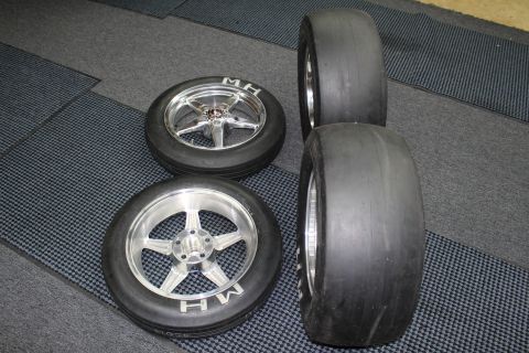 2003 Ford Crown Victoria - Two polished five-spoke wheels with M&H slicks beside two larger bare drag slicks laid out on a checkered shop floor.