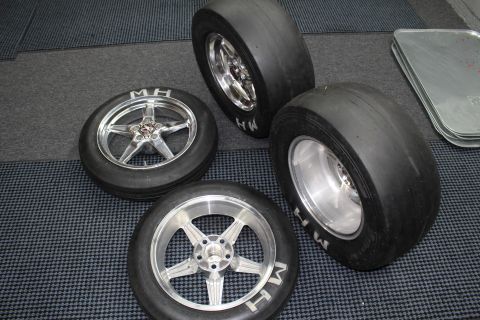 2003 Ford Crown Victoria - assortment of polished five-spoke drag wheels and mounted M&H slick tires laid out on a gray checkered floor.