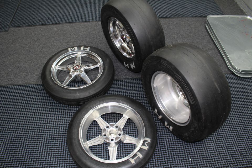Four polished aluminum drag wheels and M&H slick tires arranged on a checkered floor