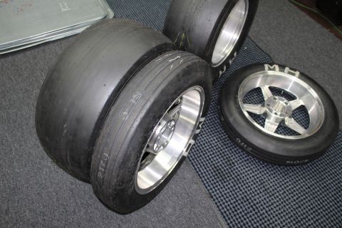 2003 Ford Crown Victoria - Several wide drag slick tires mounted on polished aluminum wheels grouped together on a gray checkered shop floor.