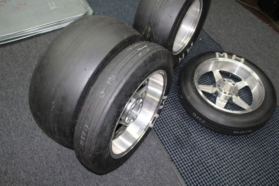 Wide drag slick tires on polished wheels grouped on a checkered shop floor