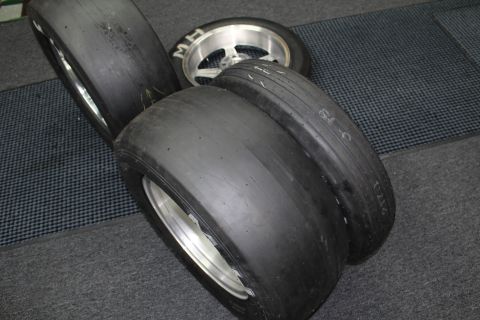 2003 Ford Crown Victoria - Several wide drag slick tires mounted on polished aluminum wheels lying together on a gray checkered shop floor.