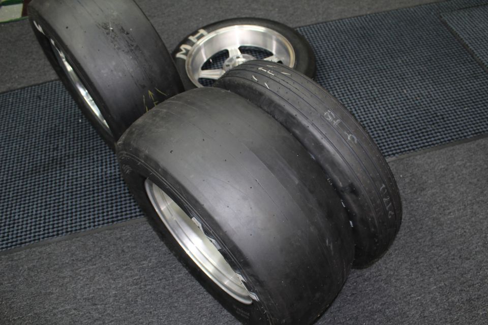 Wide drag slick tires on polished wheels lying on a checkered shop floor