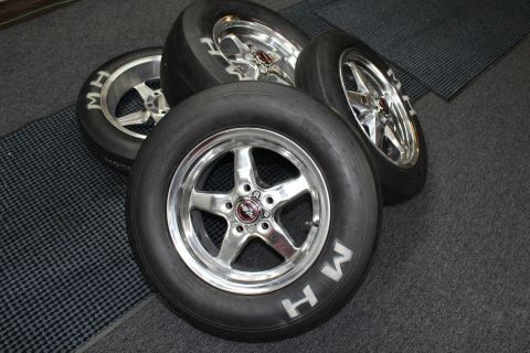 2003 Ford Crown Victoria - group of M&H Racemaster drag slicks on polished five-spoke aluminum wheels arranged on a gray checkered shop floor.