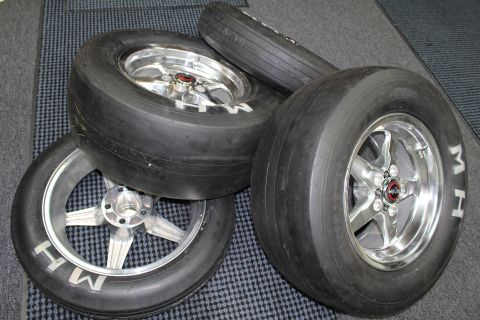 2003 Ford Crown Victoria - Several M&H slick tires on polished and brushed five-spoke aluminum drag wheels stacked together on a checkered shop floor.