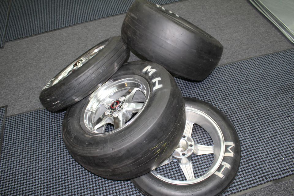 M&H drag slicks on polished five-spoke wheels arranged on a checkered shop floor