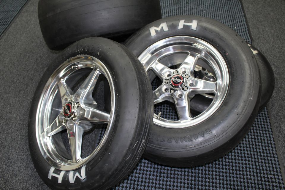 M&H drag slicks on polished five-spoke wheels with red center caps on a checkered floor
