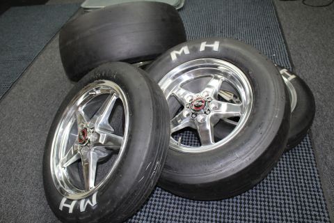 2003 Ford Crown Victoria - M&H slick tires mounted on polished five-spoke aluminum drag wheels with star-pattern faces arranged on a checkered shop floor.