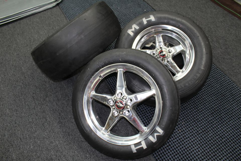 Two M&H drag slicks on polished five-spoke wheels with a bare slick behind on a checkered floor